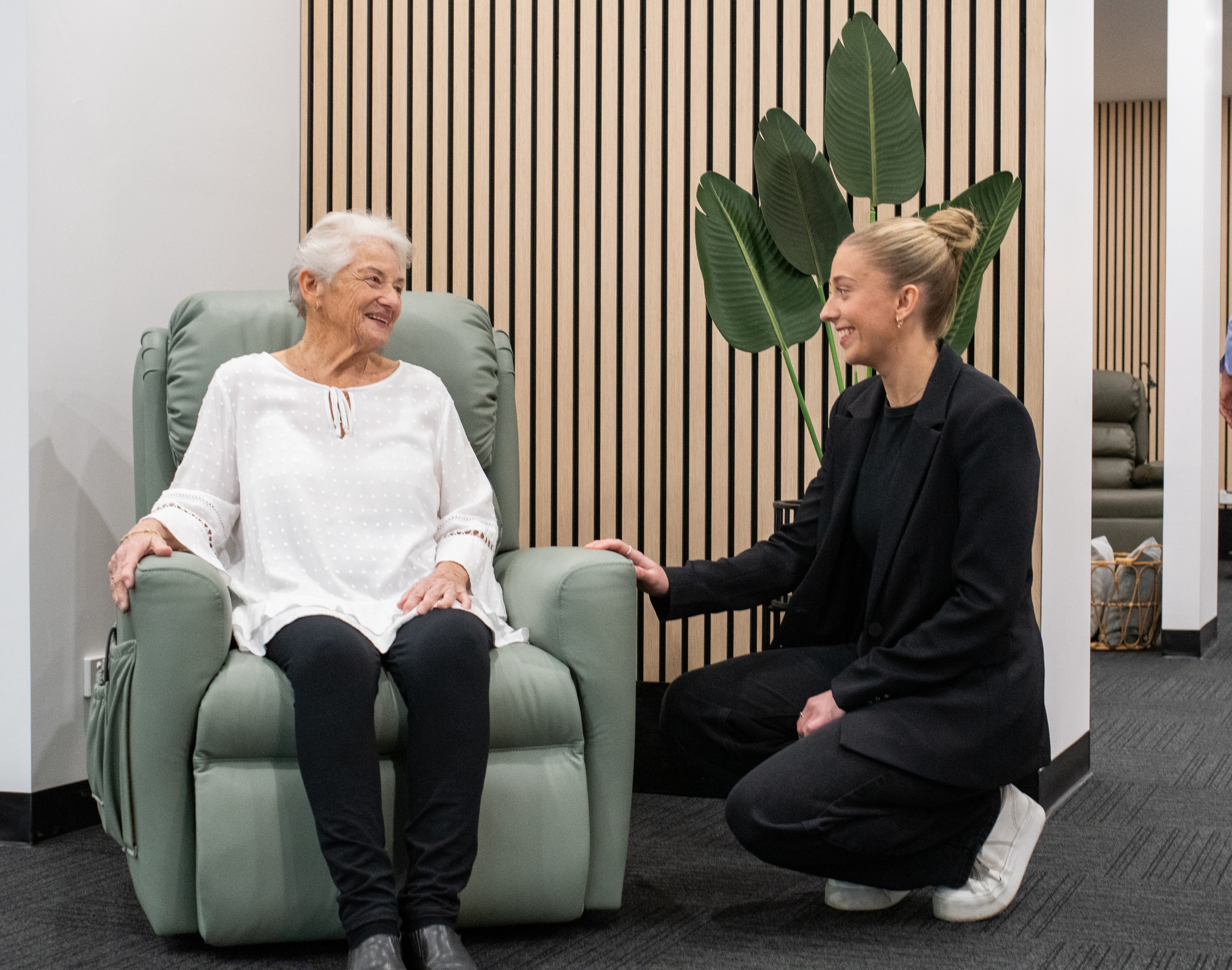 Woman seated in a green recliner speaking with a seating specialist